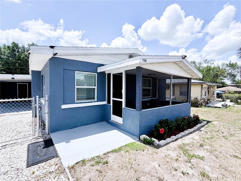 A covered porch features blue stucco walls, light wood-look tile flooring, and two wicker chairs — 1704 MARTIN L KING JR AVENUE, LAKELAND, FL