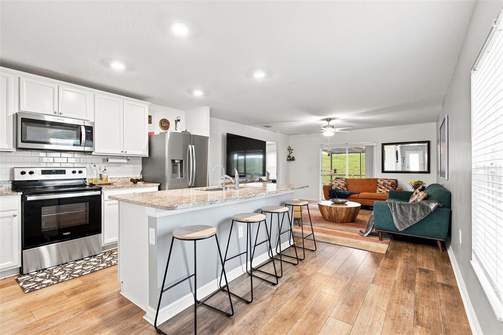 A kitchen island with granite countertops overlooks a living area with a sliding glass door — 5271 CRICKET ROAD, BROOKSVILLE, FL