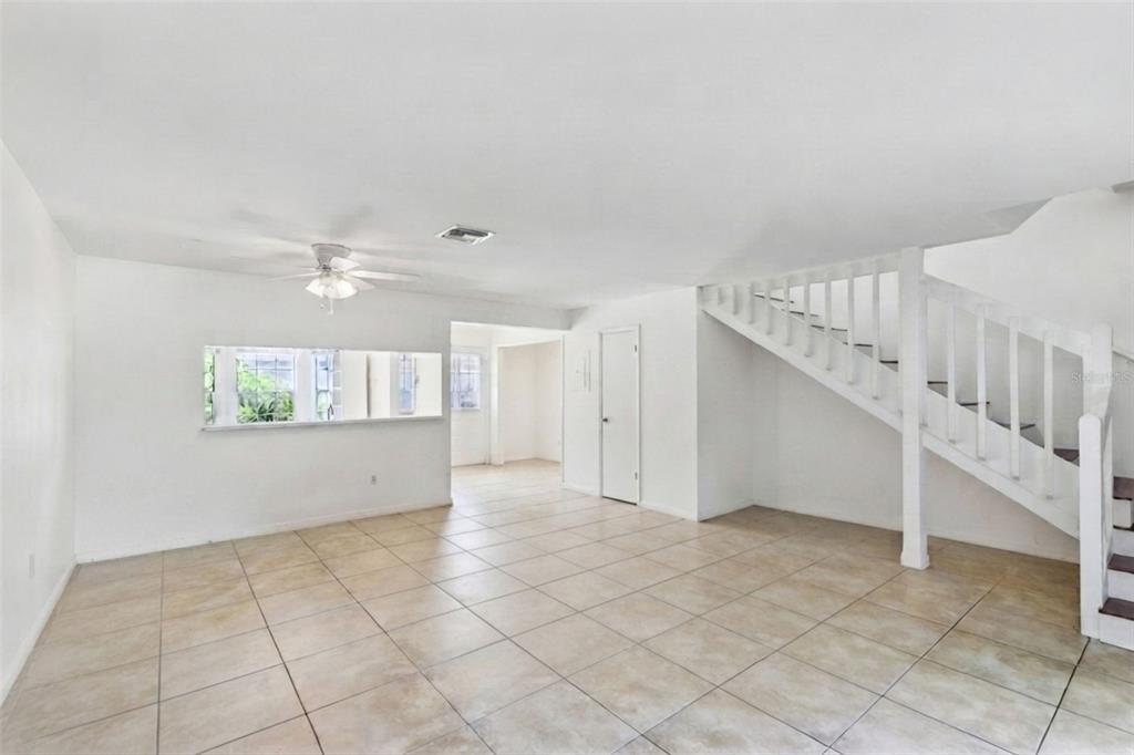 An empty room with white walls, tile flooring, a ceiling fan, and a wooden staircase — 5989 BRAEMAR PLACE UNIT 102, ORLANDO, FL