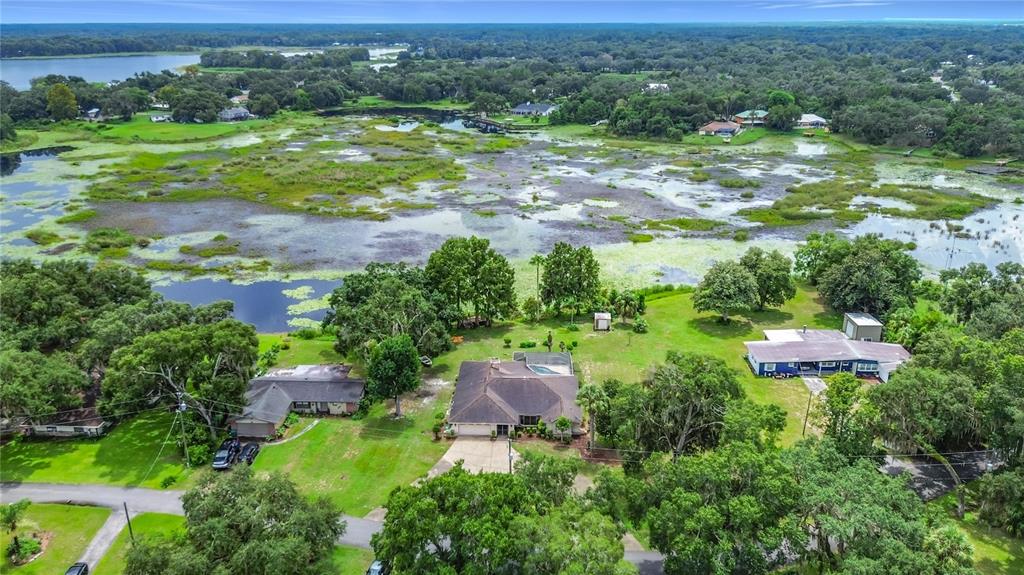 An aerial view shows three houses situated on a grassy lot bordering a large lake — 7520 E POCONO DRIVE, INVERNESS, FL