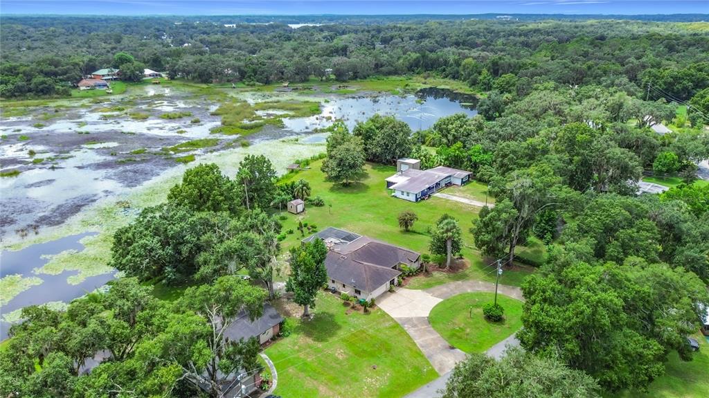 An aerial view shows two houses on a large, grassy lot bordering a marshy lake — 7520 E POCONO DRIVE, INVERNESS, FL