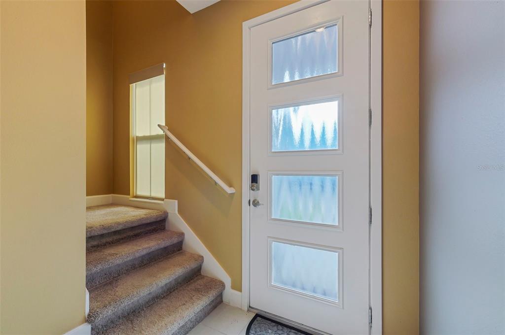 A white front door with four frosted glass panels sits beside carpeted stairs and a window — 1370 CAPTIVA COVE, SANFORD, FL