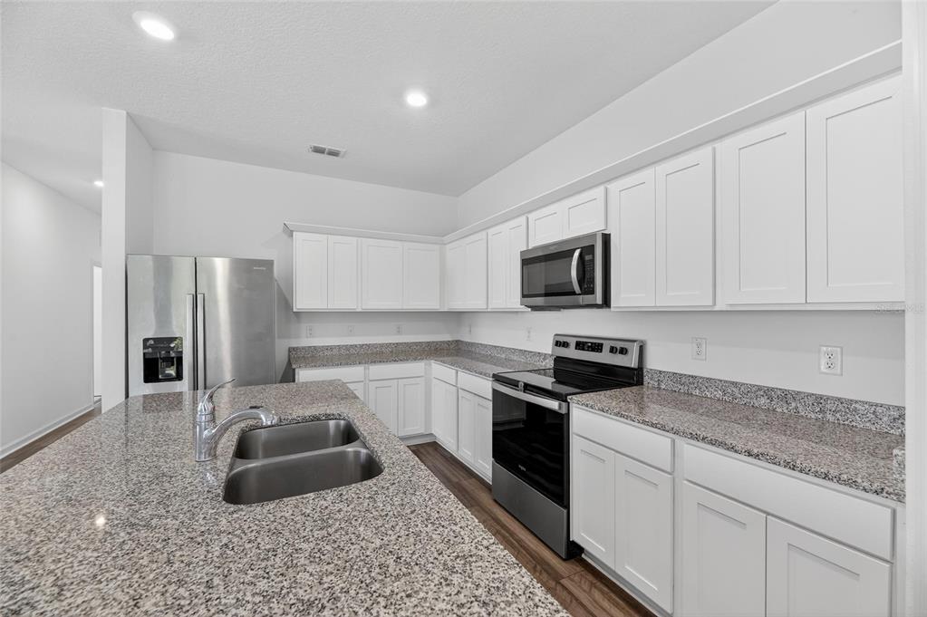 A modern kitchen features white cabinets, granite countertops, stainless steel appliances, and a central island — 1363 ANCHOR BEND DRIVE, RUSKIN, FL