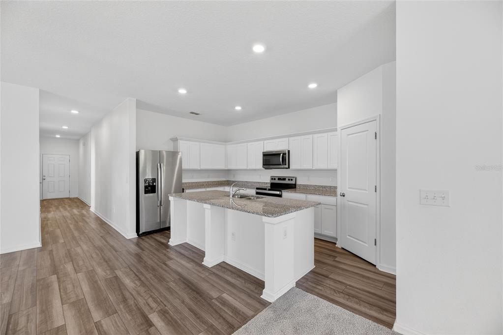 A modern kitchen features white cabinets, granite countertops, a center island, and wood-look flooring — 1363 ANCHOR BEND DRIVE, RUSKIN, FL