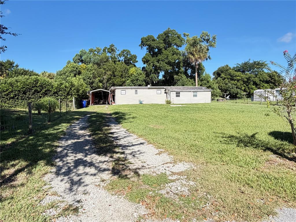 A light-colored mobile home with a carport sits on a large, grassy lot — 1814 KENTUCKY AVENUE, ST CLOUD, FL