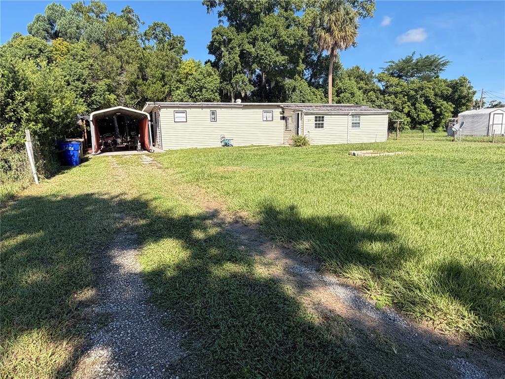 A single-story house with light siding, a metal carport, and a large grassy yard — 1814 KENTUCKY AVENUE, ST CLOUD, FL