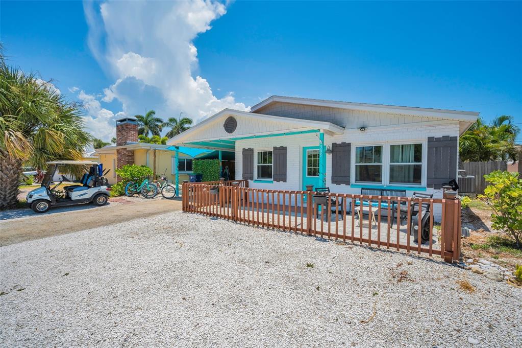 A white brick house with a wooden fence and a gravel driveway under a blue sky — 305 15TH AVENUE, INDIAN ROCKS BEACH, FL