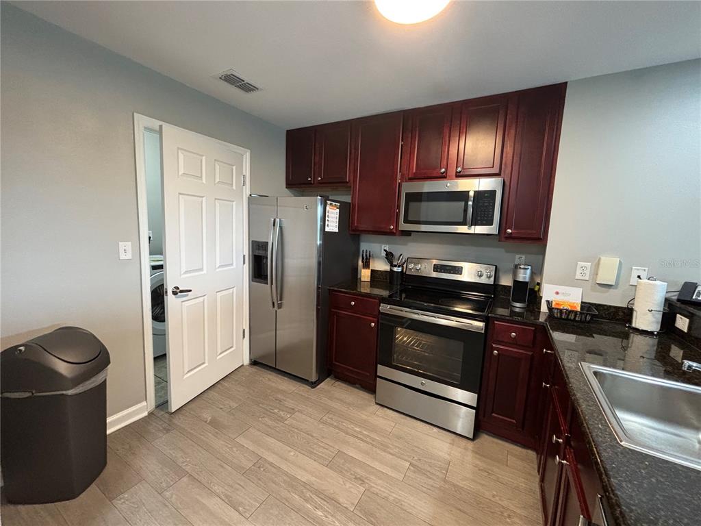 A kitchen features dark wood cabinets, stainless steel appliances, granite countertops, and light wood-look flooring — 14501 GROVE RESORT AVENUE UNIT 1420, WINTER GARDEN, FL