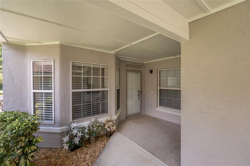 A covered entryway features a light-colored front door, beige stucco walls, and two windows — 254 GLENBRIAR CIRCLE, DAYTONA BEACH, FL