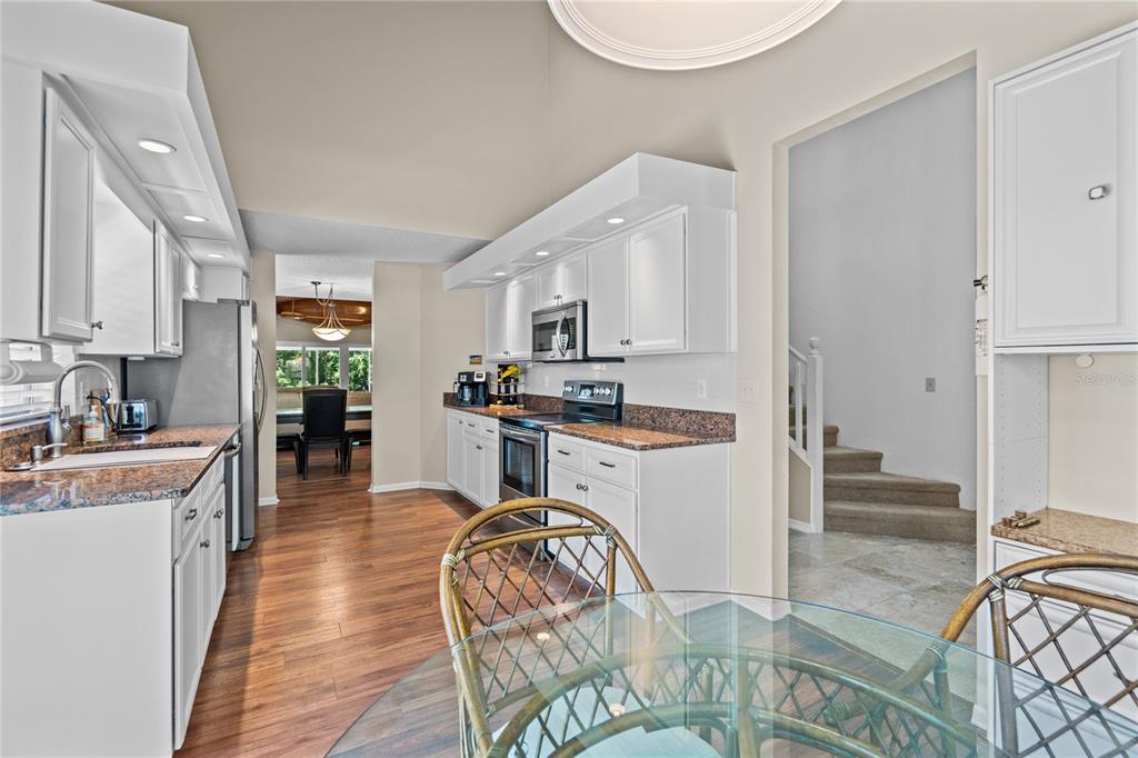A kitchen features white cabinetry, granite countertops, stainless steel appliances, and a glass-topped dining table — 254 GLENBRIAR CIRCLE, DAYTONA BEACH, FL