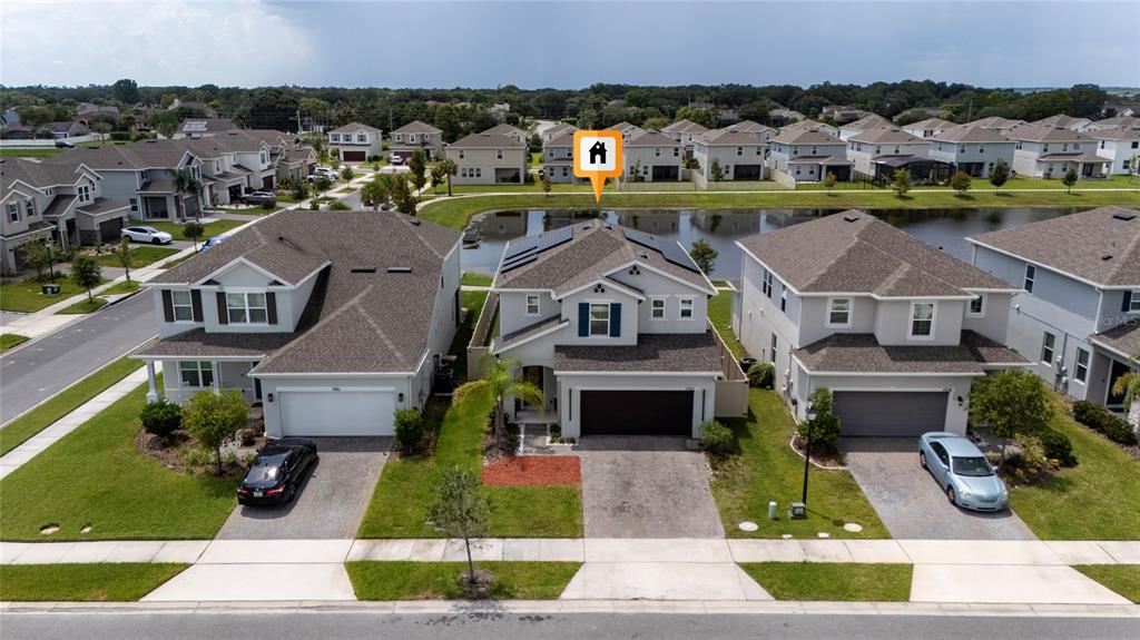 An aerial view shows a two-story suburban house with solar panels and a backyard pond — 1582 SEPAL STREET, KISSIMMEE, FL