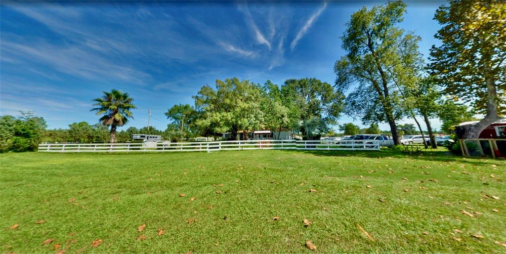 A grassy yard features a white fence, mature trees, and a house in the background — 11150 W HIGHWAY 40, OCALA, FL