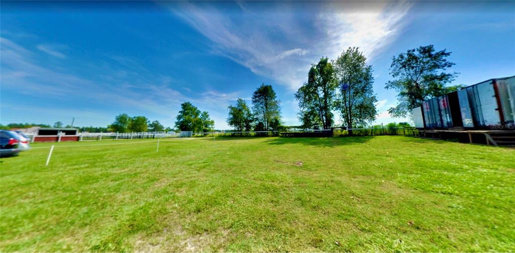 A grassy field features a white fence, scattered trees, and a large metal storage container — 11150 W HIGHWAY 40, OCALA, FL