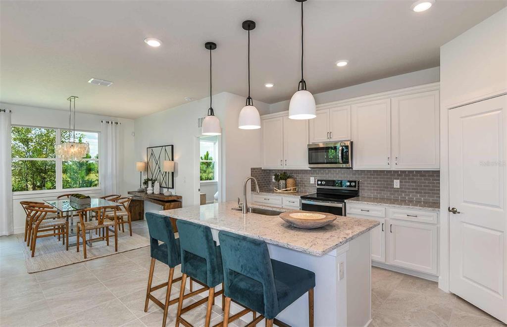 A kitchen with white cabinets, granite countertops, and a breakfast bar with three teal chairs — 14064 CALICO POINT DRIVE, RIVERVIEW, FL