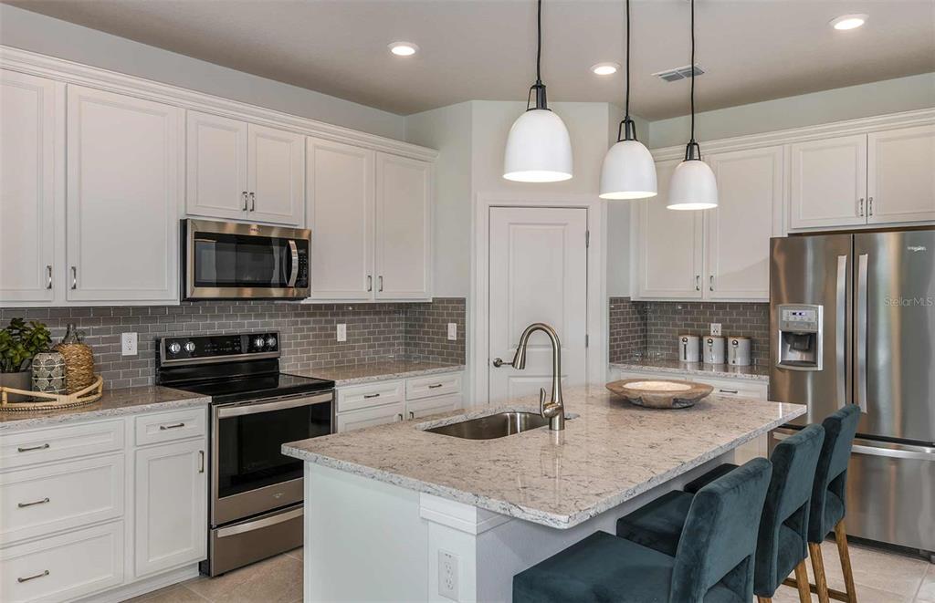 A kitchen with white cabinets, stainless steel appliances, a granite island, and gray tile backsplash — 14064 CALICO POINT DRIVE, RIVERVIEW, FL