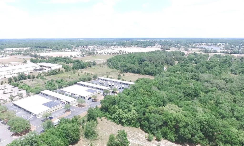 An aerial view shows commercial warehouse buildings surrounded by parking lots and dense forest — 451 ROLLING ACRES ROAD, LADY LAKE, FL