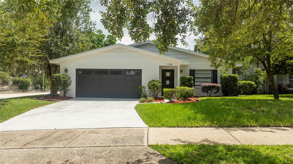A single-story house with a white exterior, a dark garage door, and a front lawn — 1124 MUNSTER STREET, ORLANDO, FL