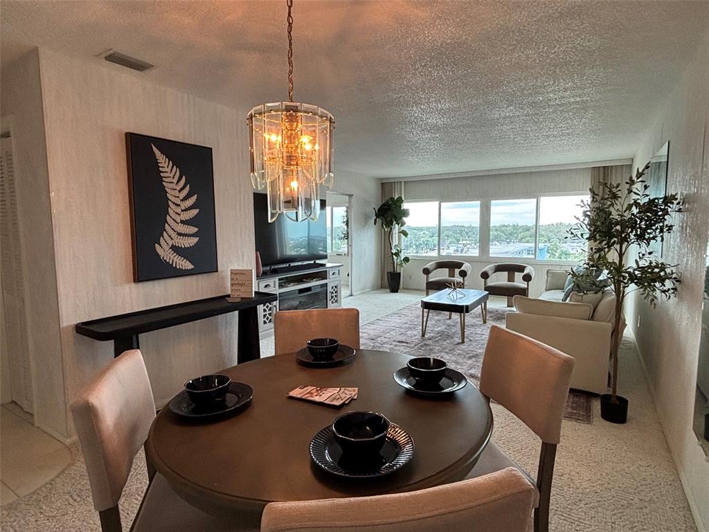 A living and dining room features a round table, sofa, and floor-to-ceiling wall mirrors — 100 BLUFF VIEW DRIVE UNIT 609A, BELLEAIR BLUFFS, FL