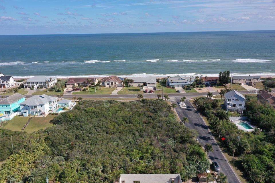 An aerial view shows a vacant, wooded lot situated between a coastal road and beach houses — 2584 N OCEAN SHORE BOULEVARD, FLAGLER BEACH, FL