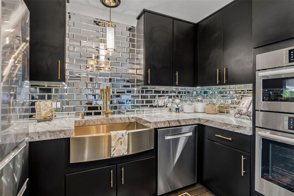 A kitchen features black cabinets, a gold farmhouse sink, and a mirrored subway tile backsplash — 5200 BRITTANY DRIVE S UNIT 1508, ST PETERSBURG, FL