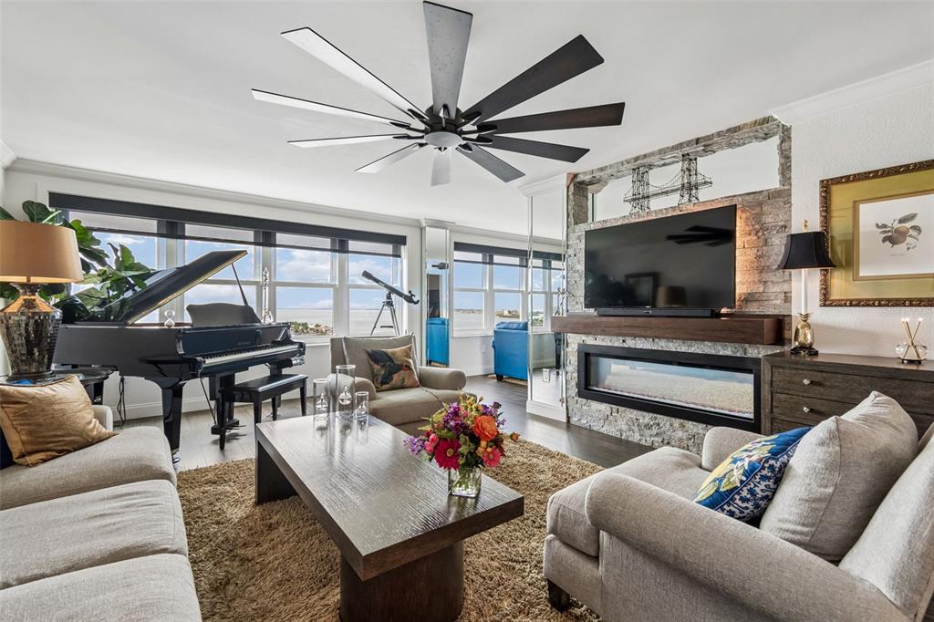 A living room features a grand piano, a fireplace with a television, and large windows — 5200 BRITTANY DRIVE S UNIT 1508, ST PETERSBURG, FL