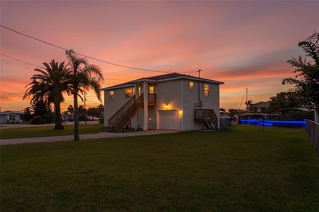 A two-story house with light siding, an attached garage, and an outdoor staircase at sunset — 6641 BOATYARD DRIVE, HUDSON, FL