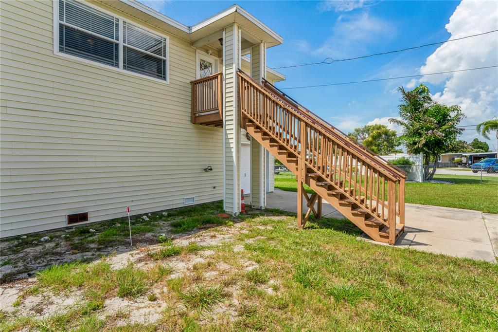 An exterior view of a house with light yellow siding and a wooden staircase — 6641 BOATYARD DRIVE, HUDSON, FL