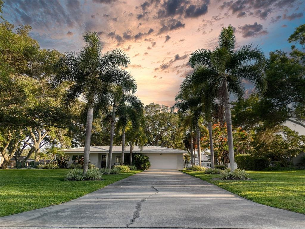 A single-story house with a concrete driveway and palm trees under a sunset sky — 5 SHORE DRIVE, DUNEDIN, FL