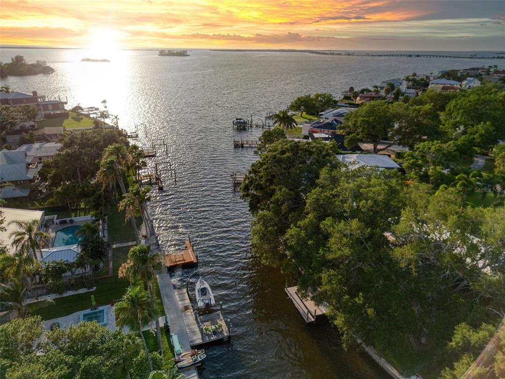 An aerial view shows a canal leading into a large body of water at sunset — 5 SHORE DRIVE, DUNEDIN, FL
