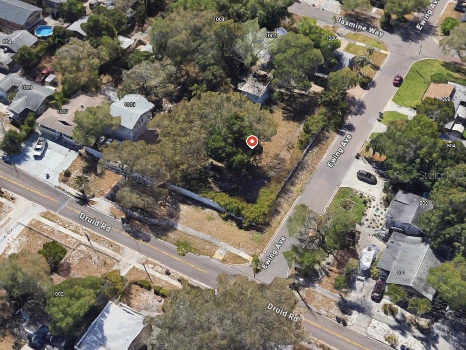 An aerial view shows a vacant, tree-covered corner lot situated between two paved roads — 1001 DRUID ROAD E, CLEARWATER, FL