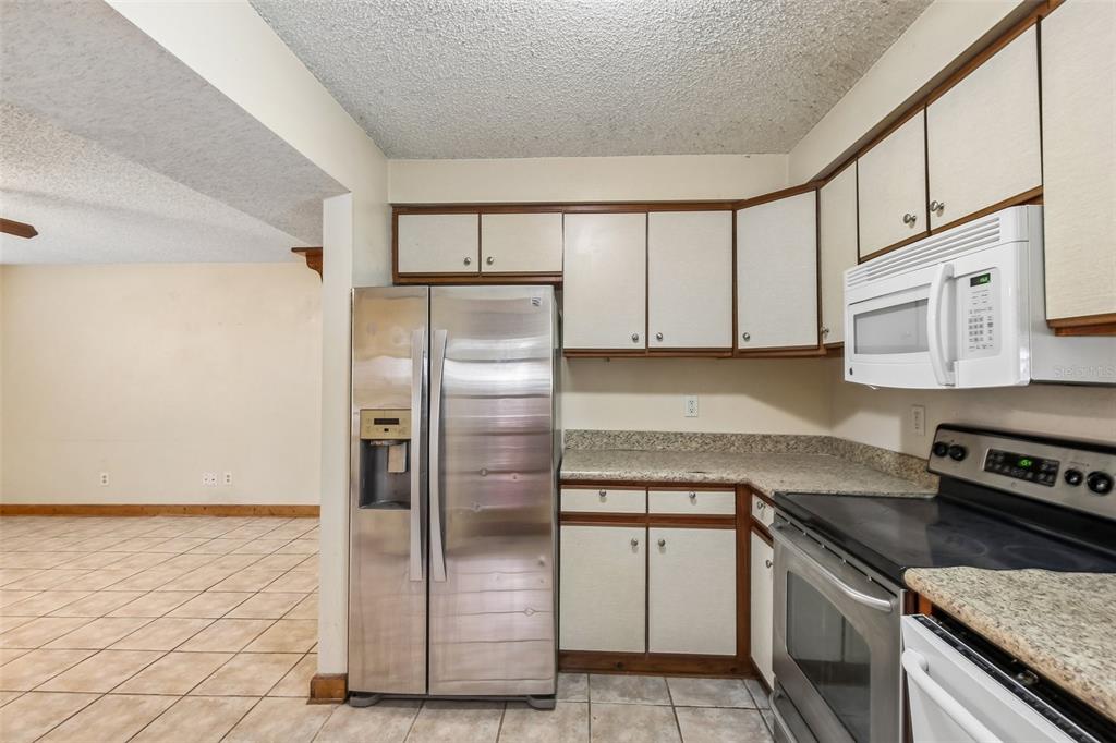 A kitchen features white cabinets with wood trim, stainless steel appliances, and beige tile flooring — 2702 49TH STREET S, GULFPORT, FL