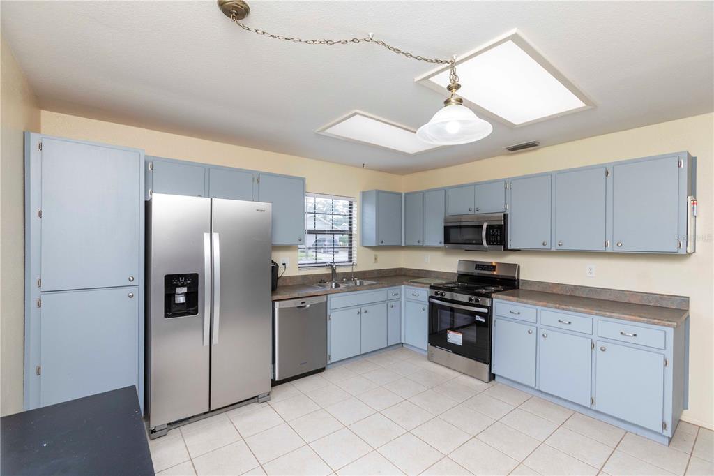 A kitchen with light blue cabinets, stainless steel appliances, and beige tile flooring — 8900 WHISTLER WAY, HUDSON, FL