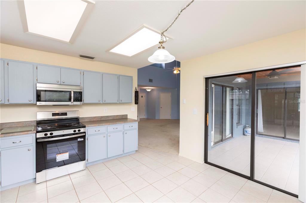 A kitchen with light blue cabinets, stainless steel appliances, and tile flooring leads to a patio — 8900 WHISTLER WAY, HUDSON, FL