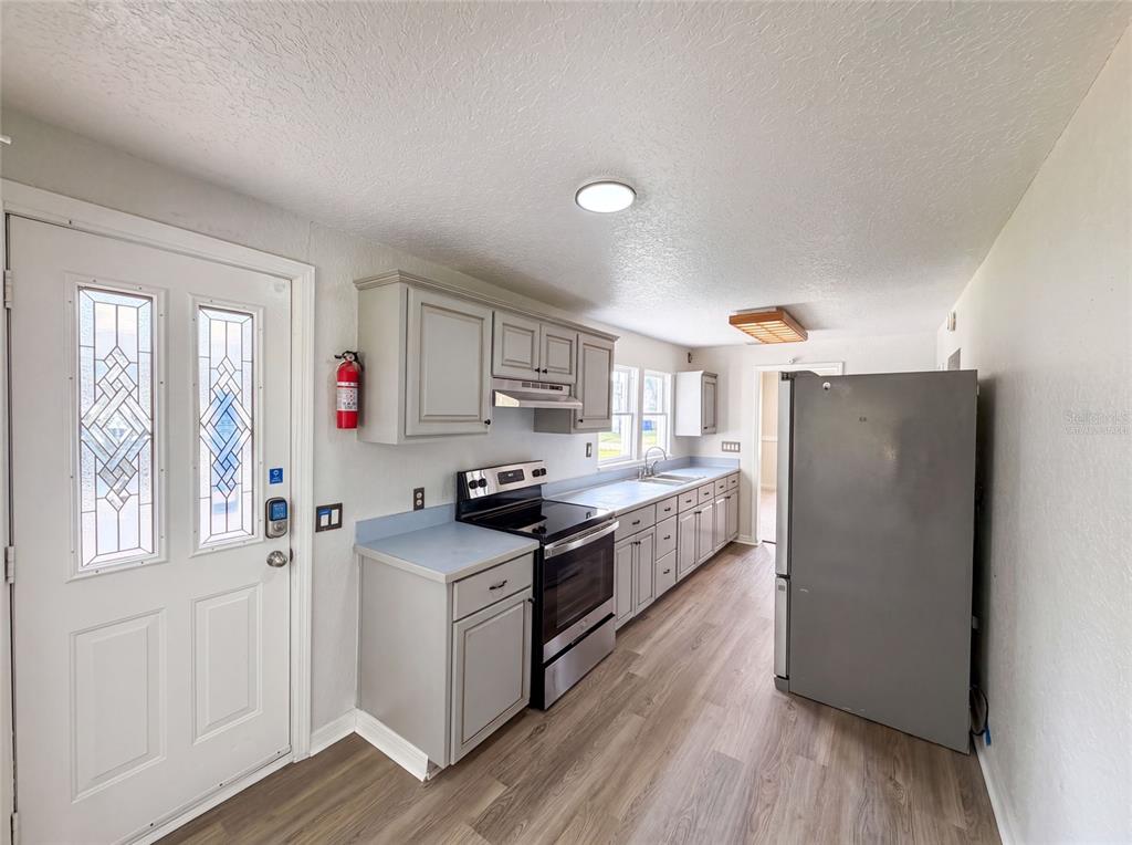 A kitchen features light gray cabinets, stainless steel appliances, blue countertops, and wood-look flooring — 718 ALABAMA AVENUE, ST CLOUD, FL