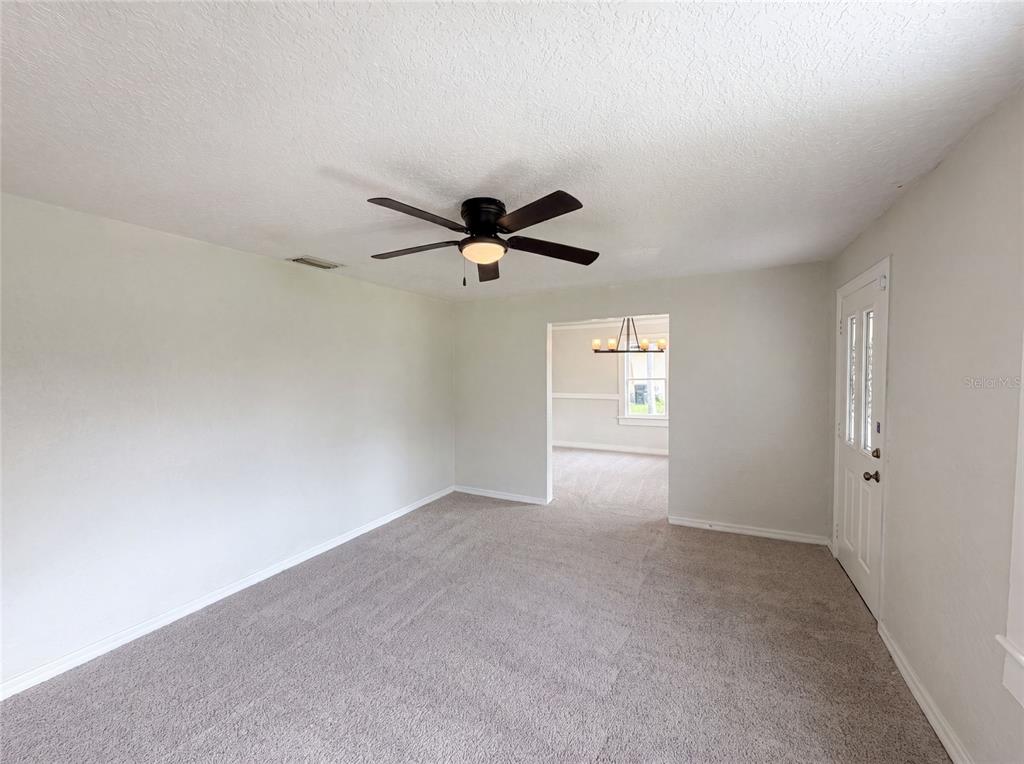 A carpeted living room features a ceiling fan and a doorway leading to another room — 718 ALABAMA AVENUE, ST CLOUD, FL
