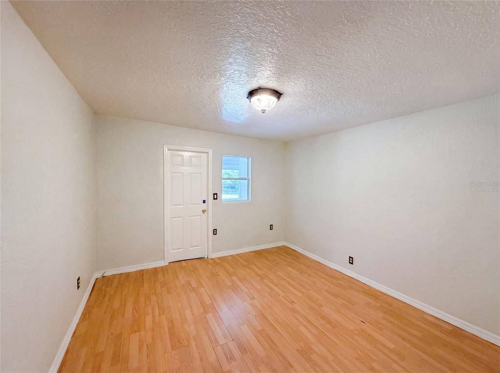 An empty room with light wood-look flooring, white walls, a single window, and a door — 718 ALABAMA AVENUE, ST CLOUD, FL