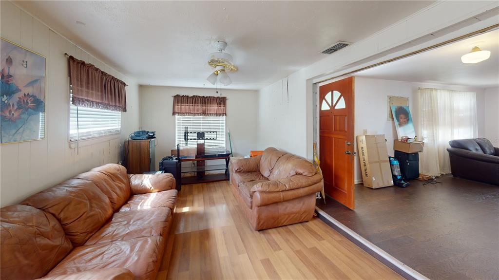 A living room features wood-look flooring, two brown leather sofas, and a wooden front door — 1721 W NORTH B STREET, TAMPA, FL