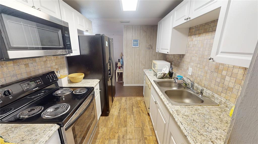 A galley kitchen features white cabinets, granite countertops, a black stove, and a black refrigerator — 1721 W NORTH B STREET, TAMPA, FL