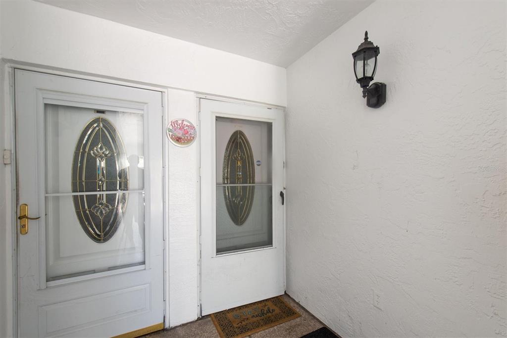 A white exterior entryway features two glass-paneled storm doors and a wall-mounted outdoor light fixture — 1655 S HIGHLAND AVENUE UNIT J194, CLEARWATER, FL