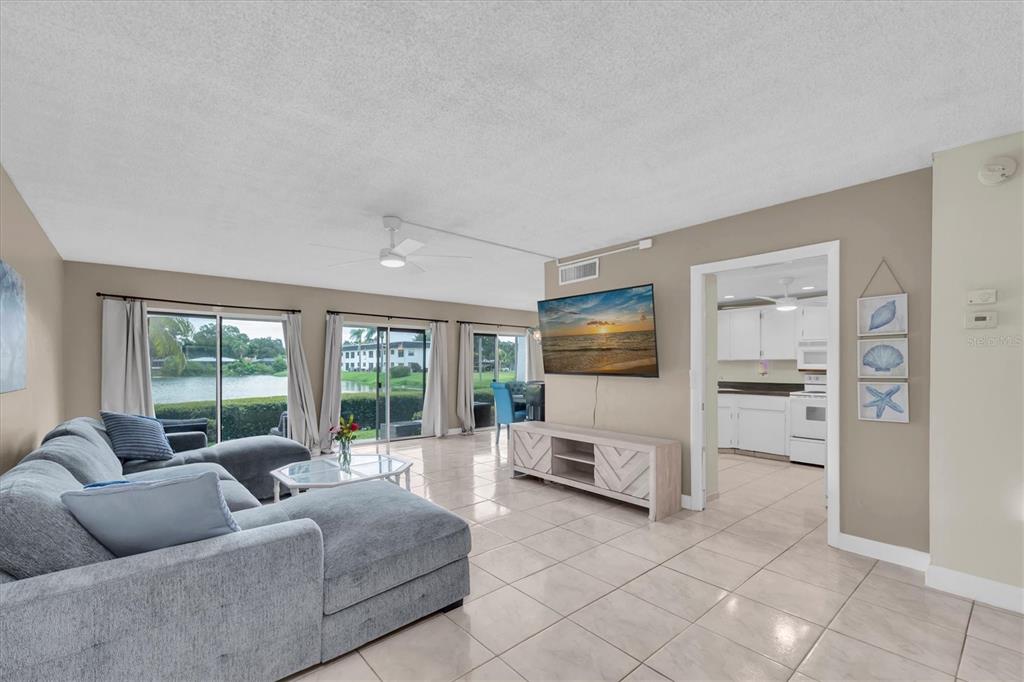 A living room with a grey sectional sofa, tile flooring, and a view of water — 1655 S HIGHLAND AVENUE UNIT J194, CLEARWATER, FL