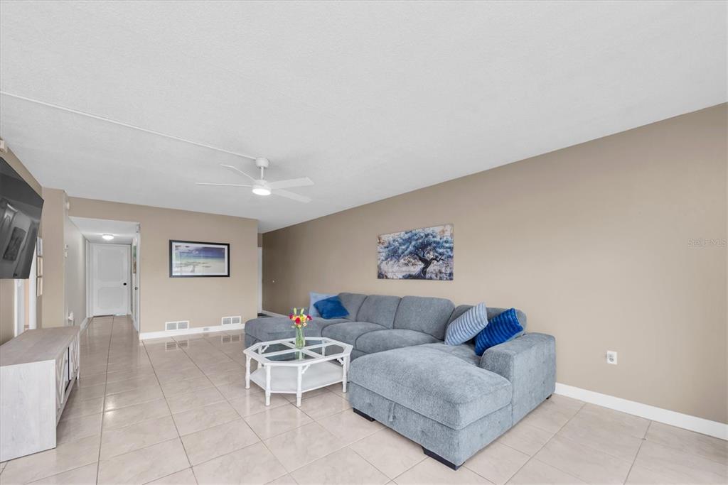 A living room features a grey sectional sofa, a white coffee table, and tiled flooring — 1655 S HIGHLAND AVENUE UNIT J194, CLEARWATER, FL