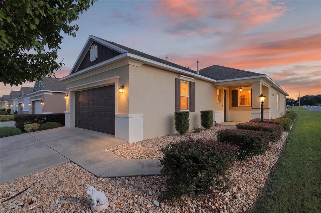 A single-story house with a tan stucco exterior, a dark garage door, and gravel landscaping — 9947 SW 100TH TERRACE ROAD, OCALA, FL