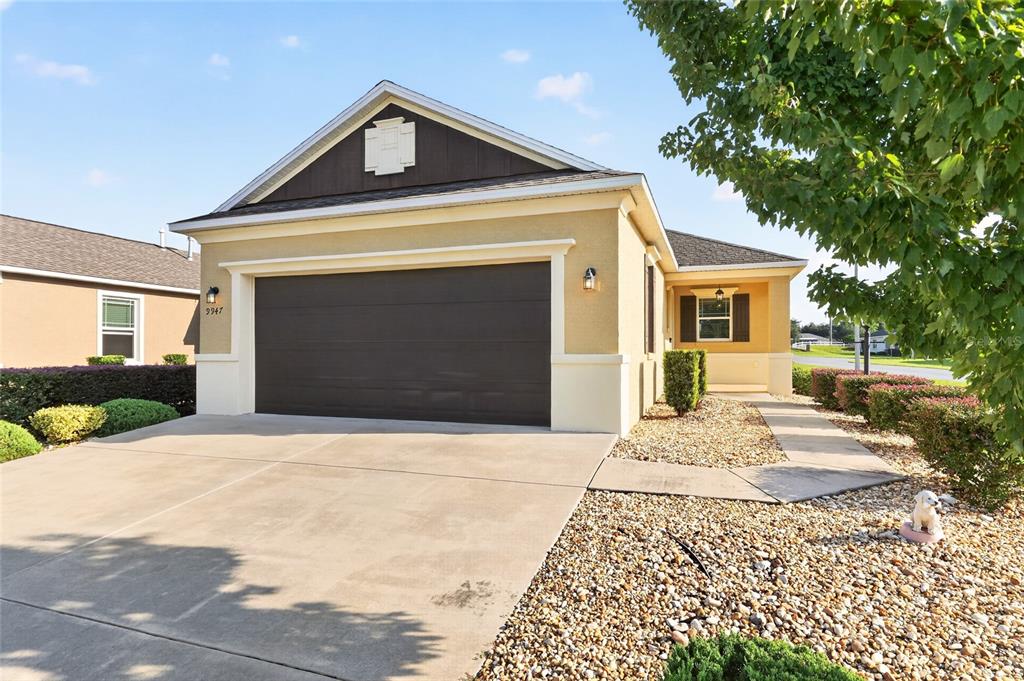 A tan single-story house features a dark brown garage door and a gravel front yard — 9947 SW 100TH TERRACE ROAD, OCALA, FL