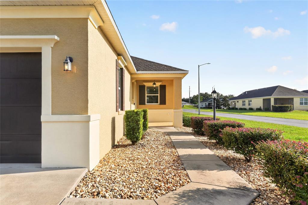 A tan house exterior features a concrete walkway, gravel landscaping, and a dark garage door — 9947 SW 100TH TERRACE ROAD, OCALA, FL
