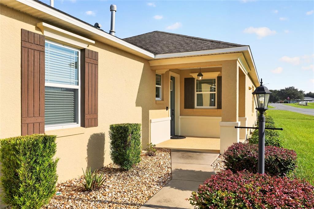 The exterior of a tan house features a covered porch, brown shutters, and landscaping — 9947 SW 100TH TERRACE ROAD, OCALA, FL