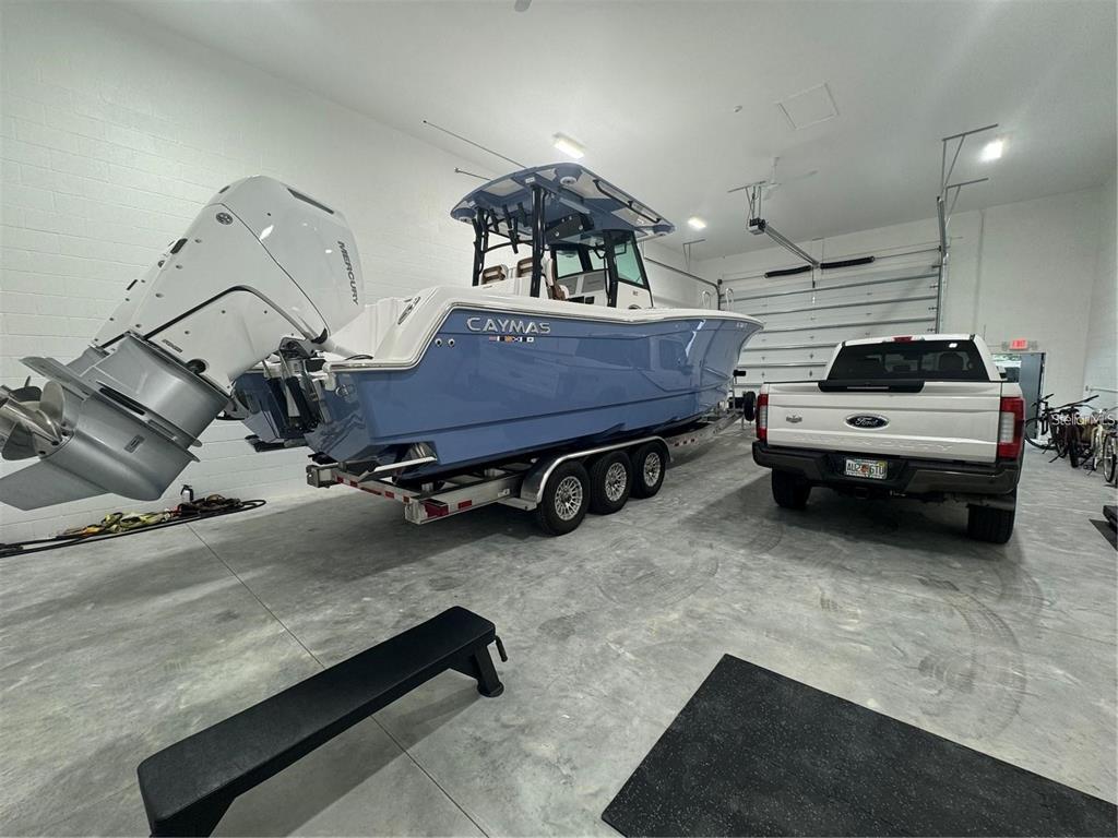 A light blue Caymas boat on a trailer is parked inside a spacious white garage — 25155 AIRPORT ROAD UNIT D3, PUNTA GORDA, FL