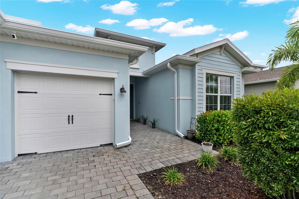 A light blue house exterior features a white garage door and a paved walkway entrance — 17661 FALLEN BRANCH WAY, PUNTA GORDA, FL