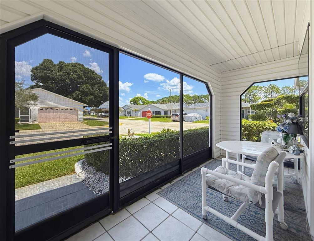 A screened-in porch with white siding, tile flooring, and outdoor furniture overlooks a suburban street — 1804 MASTERS LANE, LAKELAND, FL