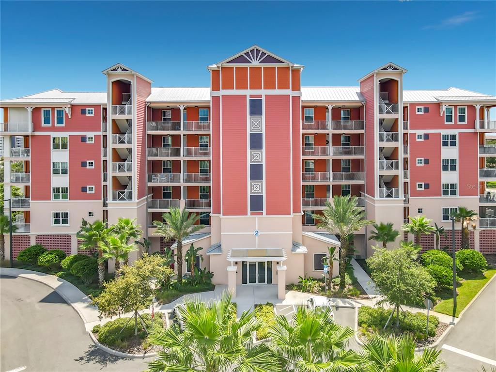 An exterior view of a multi-story, coral-colored apartment building with balconies and palm trees — 2 RIVERWALK DRIVE UNIT 404, NEW SMYRNA BEACH, FL