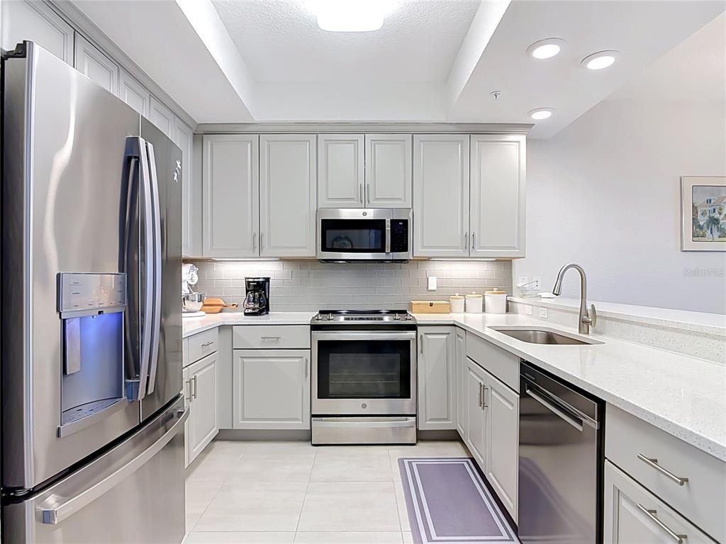 A modern kitchen features light gray cabinets, stainless steel appliances, and white quartz countertops — 2 RIVERWALK DRIVE UNIT 404, NEW SMYRNA BEACH, FL